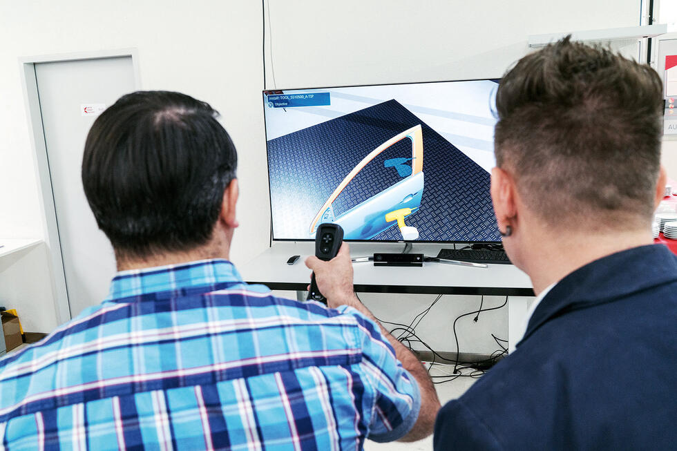 Two people in front of a screen with a joystick in their hand