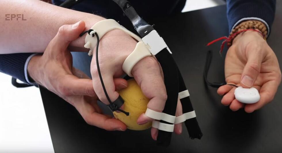 A hand with an exoskeleton holds a small ball