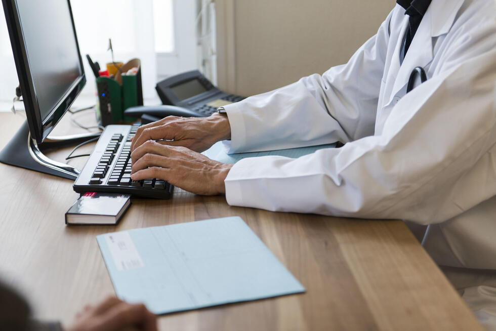 A medical professional sits at the computer and types