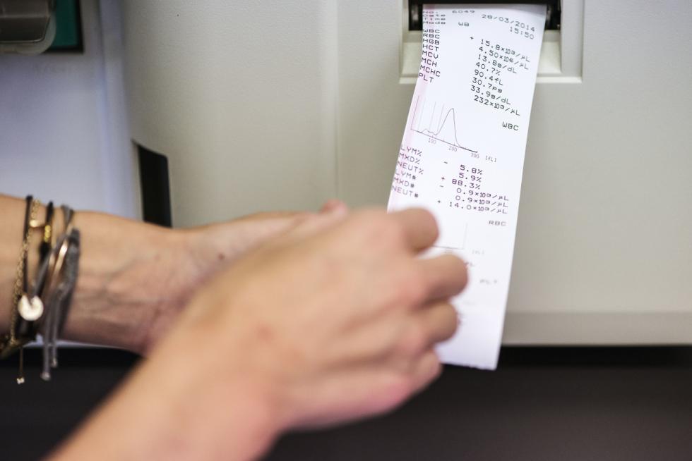 Hands reaching for a paper with blood values coming out of a printer