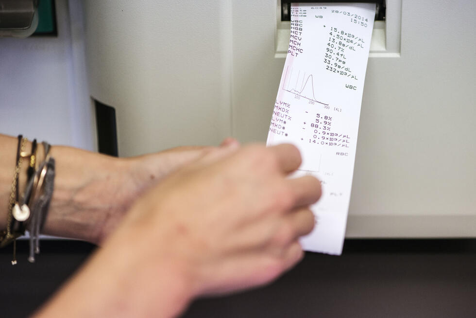 Hands reaching for a paper with blood values coming out of a printer